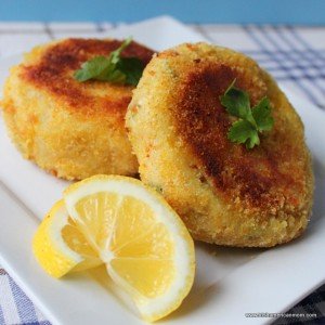 Two cod fish cakes on a plate with lemon wedges
