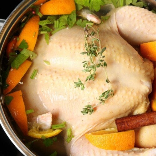 An uncooked turkey in a pot with vegetables and herbs for brining