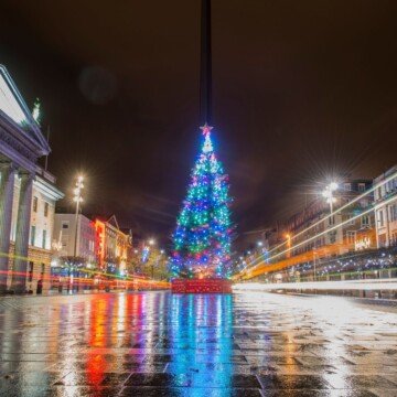 A blue illuminated Christmas tree reflects on a wet city street