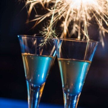 Sparklers glisten at night over two glass flutes of champagne