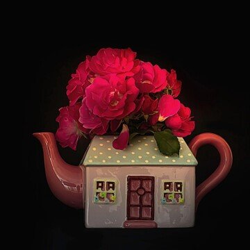 A teapot shaped like a cottage with red flowers
