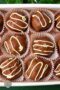 Assorted chocolate truffles topped with white drizzle in pink paper cups on a serving tray.