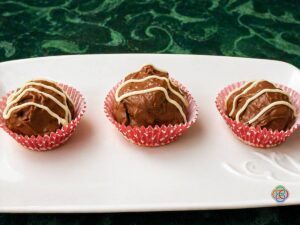 Three chocolate truffles in pink cupcake liners lined up on a white platter, drizzled with white chocolate.