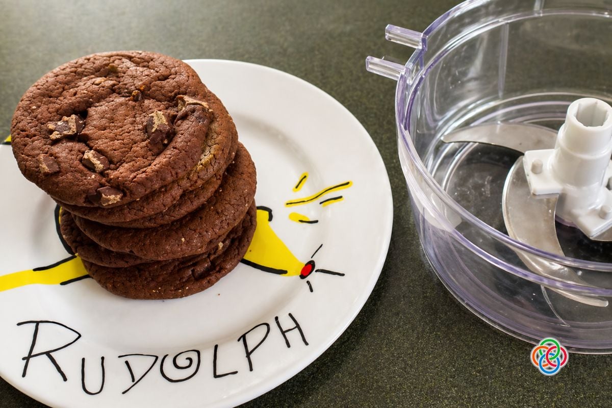 Stack of chocolate cookies on a plate beside a food processor, ready to be blended into crumbs for making no bake chocolate truffles.