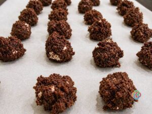 Rows of chocolate truffles on parchment paper, each bite-sized and crumbly-coated with a dark cocoa crust