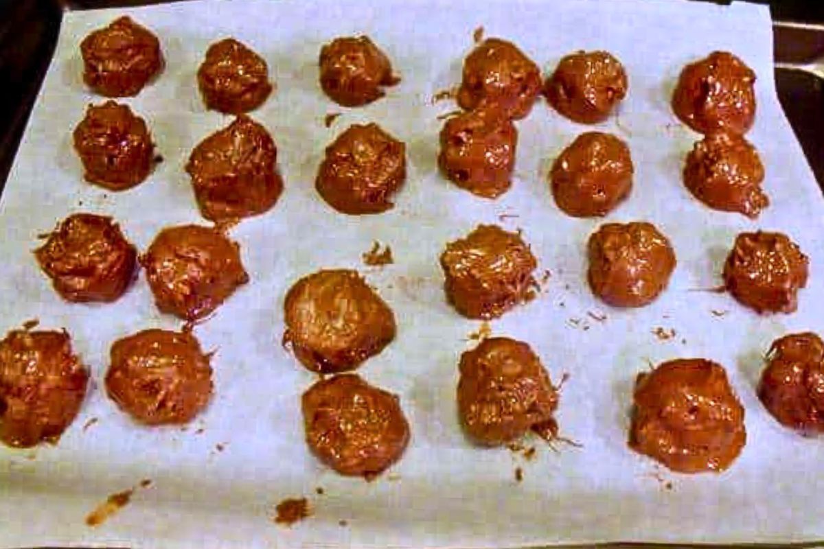 Chocolate truffles coated in melted chocolate arranged on a parchment-lined baking tray, setting before serving in a no bake Baileys truffle recipe.