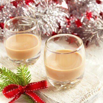 Two glasses of Irish cream beside Christmas decorations on a table