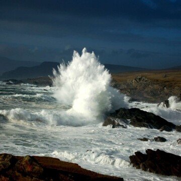 White spume rises in the air as a wave crashes against a rock on a shoreline