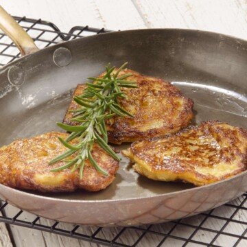 Three potato pancakes in a silver skillet with a thyme sprig