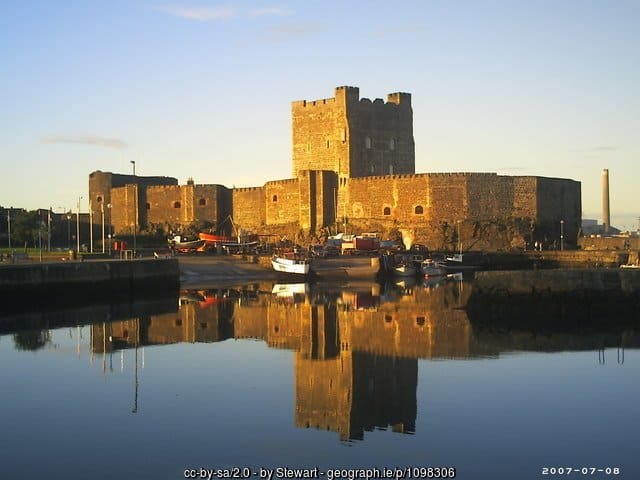 Carrickfergus Castle | Irish American Mom A stone castle or keep with a fortified wall by the sea and lit by the setting sun