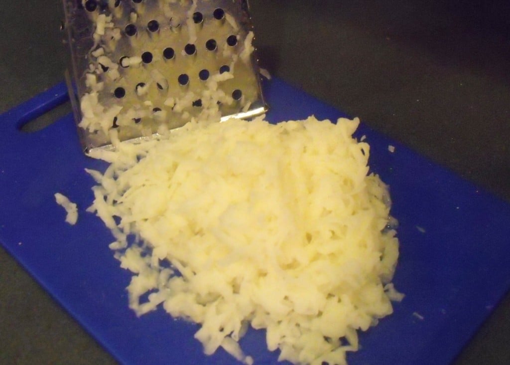 A chopping board with freshly grated potato beside a hand held grater