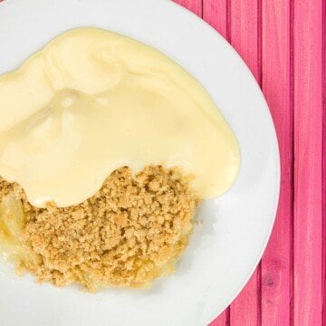 A white bowl with apple crumble and yellow hot custard sauce