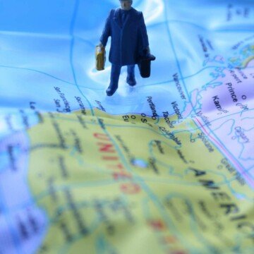 A man holding luggage standing on blue ocean beside a map of the United States