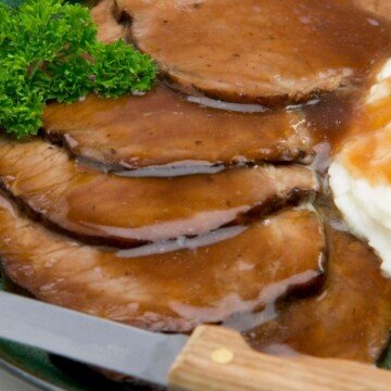 Slices of roast beef with gravy beside a knife