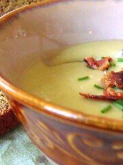 A brown bowl with potato and leek soup with a bacon and chive garnish