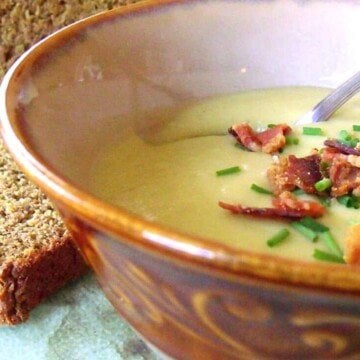 A brown bowl with potato and leek soup with a bacon and chive garnish