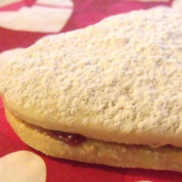 A heart shaped cookie with jam and a dusting of powdered sugar on a red napikn