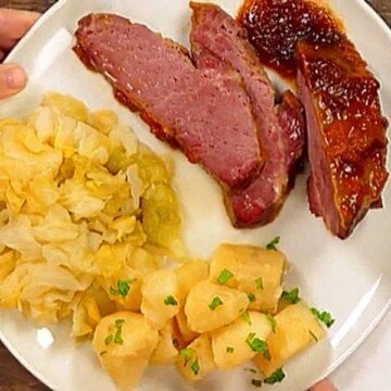 A white plate with a serving of apricot glazed corned beef, cabbage and boiled potatoes with parsley garnish