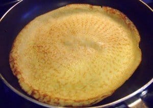 A pancake in a pan with the upper side cooked and tinged brown
