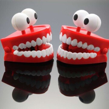 Red toy dentures with eyes facing each other on a reflective surface