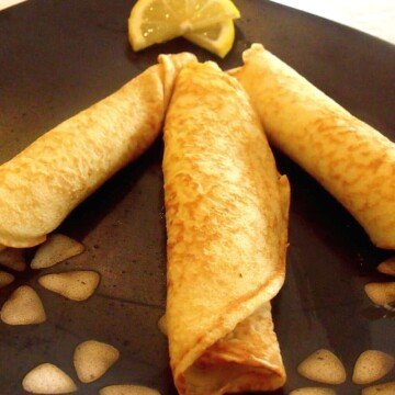 Three rolled crepes on a plate with a lemon slice