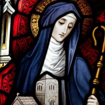 A woman in a nun's habit holding a staff and a building model