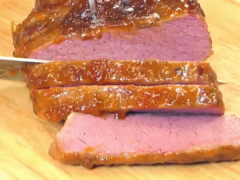 Slicing an apricot glazed corned beef brisket | Irish American Mom A cooked glazed brisket of corned beef being sliced on a wooden chopping board