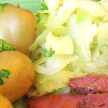 A serving of chopped boiled cabbage on a plate with potatoes in their skins and corned beef