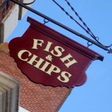 A red shop sign for fish and chips hanging on a building