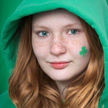 A red haired girl with green eyes and a shamrock painted on her cheek