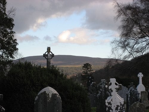 Celtic Cross In Glendalough Stone cross in a cemetery by a mountain