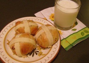 A glass of milk with three hot cross buns on a plate