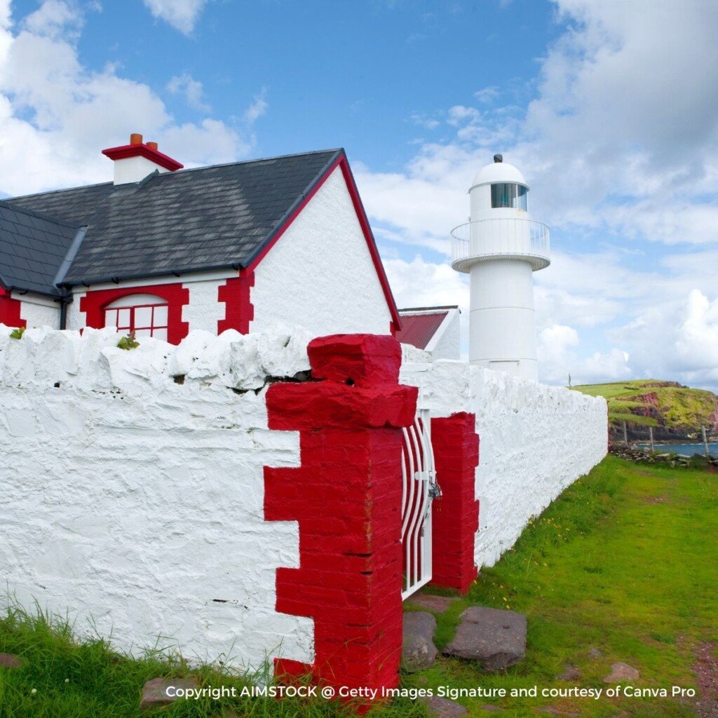 Cottage behind a red and white wall with a lighthouse in the distance