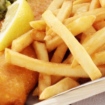 Close up of potato chips or French fries with a wedge of lemon and battered fish
