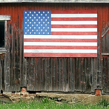 An American flag wooden art piece hanging on the side of an old wooden structure