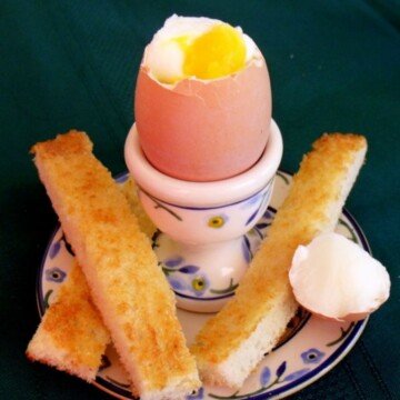 Boiled egg with the top off in an egg cup with toast sticks