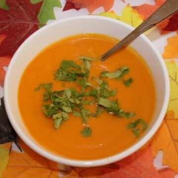 A bowl of orange carrot and coriander soup with fall leaves