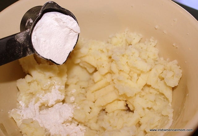 Adding flour to mashed potatoes for tatty scone | Irish American Mom Adding flour to mashed potatoes in a bowl for making Irish potato cakes