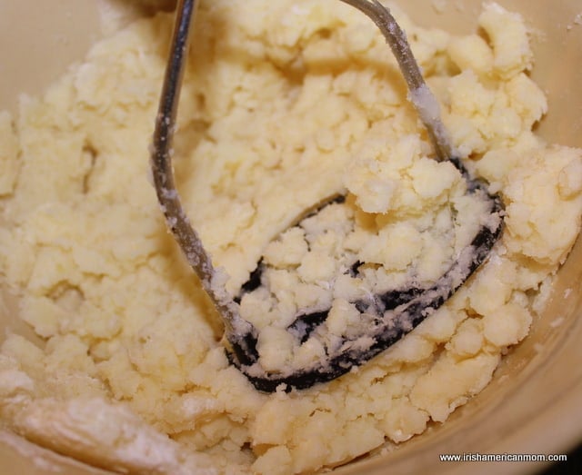 Mashing potato and flour together for tatty scone | Irish American Mom using a potato masher to mix flour and mashed potato together to make a dough for potato cakes
