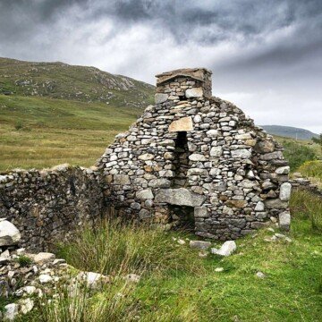 Stone cottage in ruins on the side of a sgrassy slope
