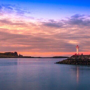 Sunset over water by a lighthouse beacon
