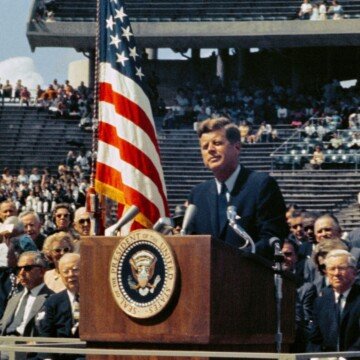 A man beside a podium and a flag