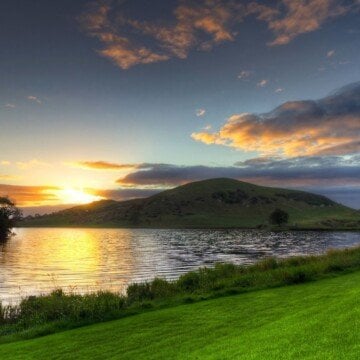 The sun sets over a hill by a lake