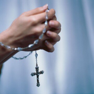 Rosary beads clasped in a woman's hands