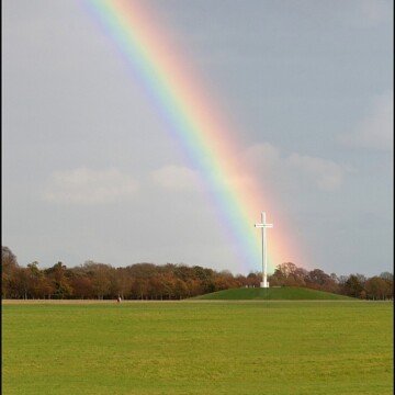A rainbow falling on a white cross in a green field