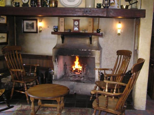 Turf Fire in the Bushmills Inn | Irish American Mom An open turf fire in a grate surrounded by three wooden chairs and a small table