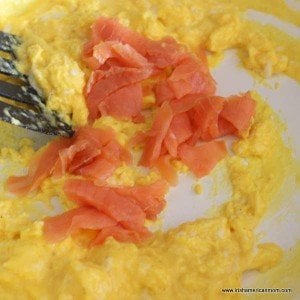 Pieces of smoked salmon being added to partially cooked scrambled egg