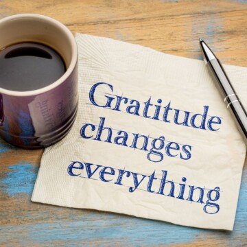 A cup of coffee beside a napkin with text and a pen on a wooden surface