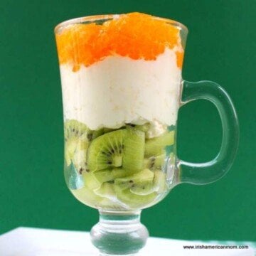 Green fruit with cream and orange fruit in a glass with a handle
