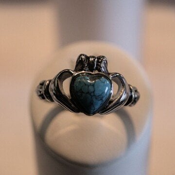 A ring with a heart stone in the center, clasped by hands and topped with a crown